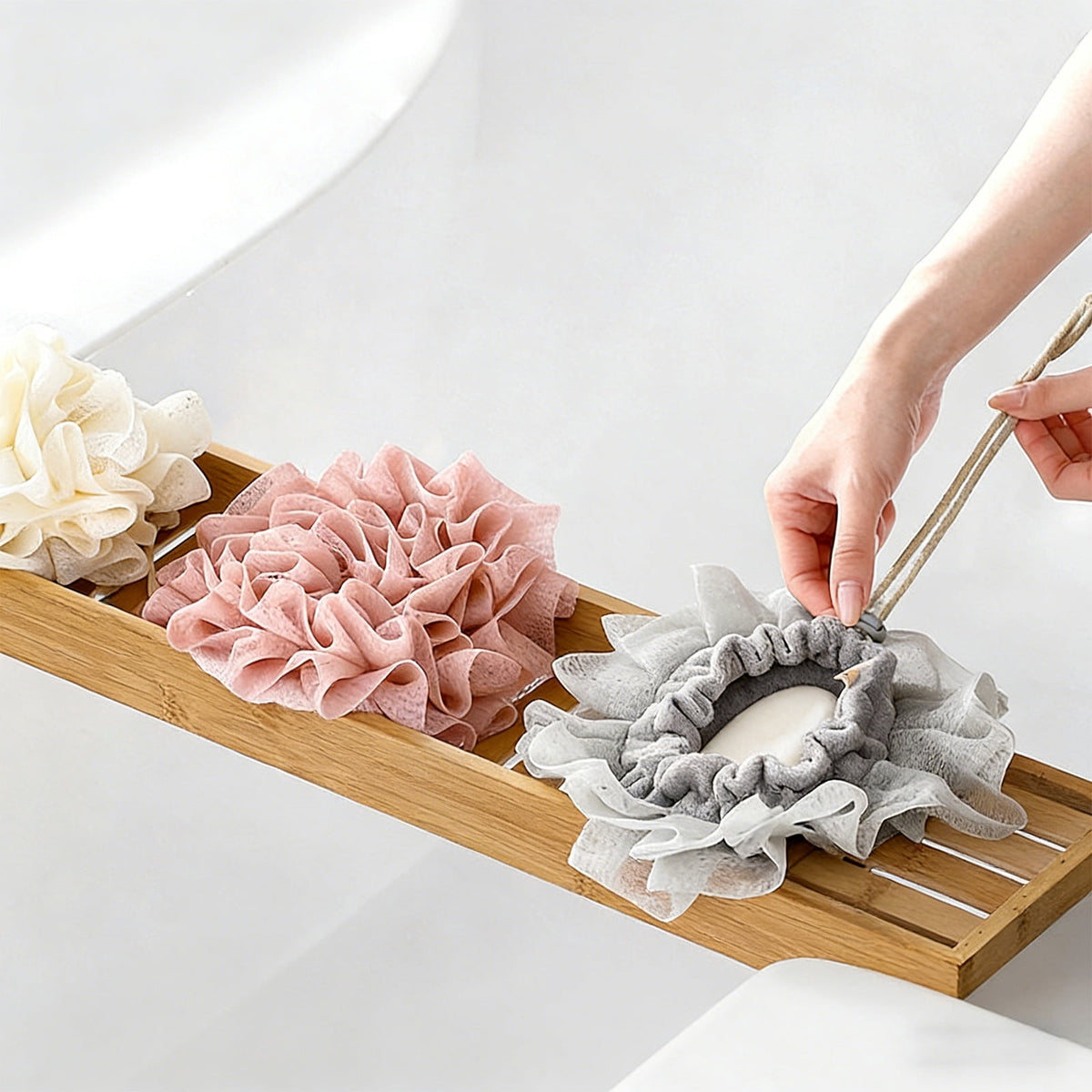 Beige gray and pink bath puffs displayed beside a bathtub